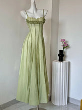 Green dress on a mannequin against a plain wall with a vase of flowers on a pedestal.
